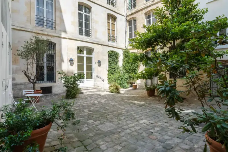 Cour pavée d'un immeuble parisien, avec un petit olivier et une table. Idéal pour un projet de déménager à Paris et profiter de la douceur de vivre.