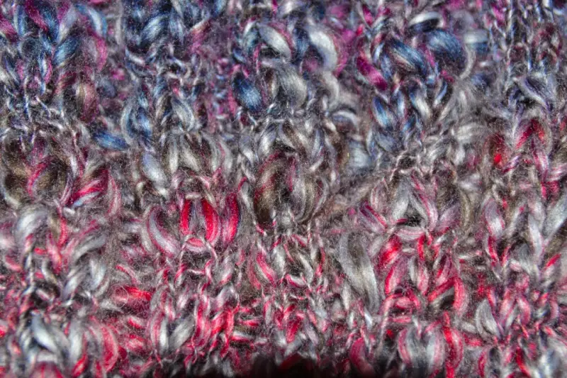 Detaljerad vy av en stickad tubhalsduk i garn med färger som grått, rosa och blått. Mönstret är en enkel slätstickning.