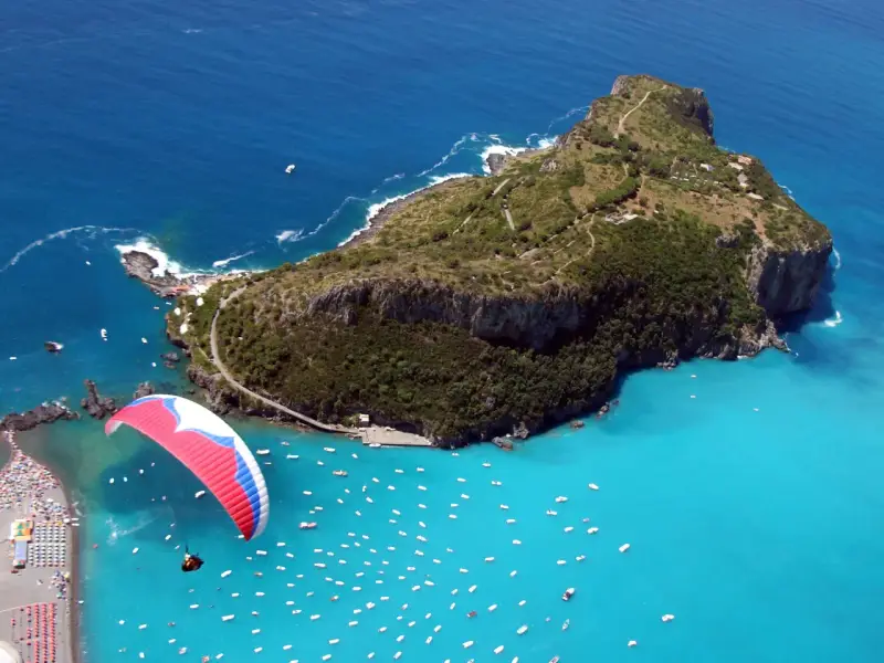 Parapendio su un mare turchese vicino a isole calabresi, con una spiaggia affollata e tante barche.