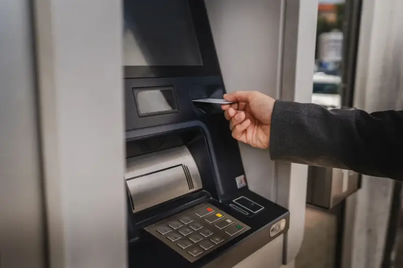Dłoń wsuwa kartę do bankomatu, by sprawdzić, ile można wypłacić.