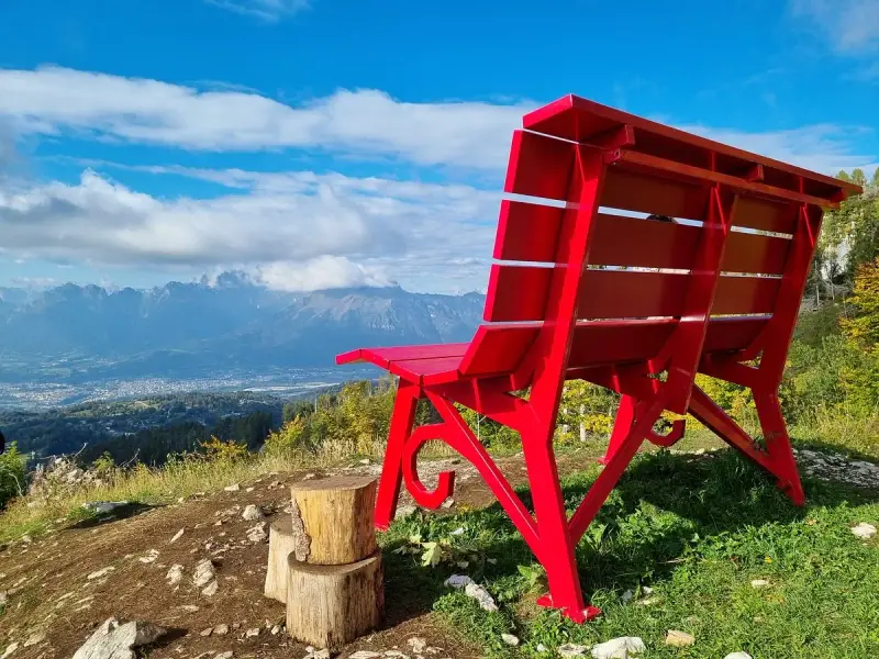 La panchina gigante sul Nevegal, rossa e imponente, domina un panorama mozzafiato di montagne e vallate sotto un cielo azzurro.