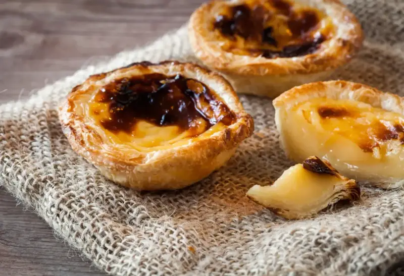 Tre krämiga portugisiska bakelser med karamelliserad yta, en klassiker inom portugisisk mat.