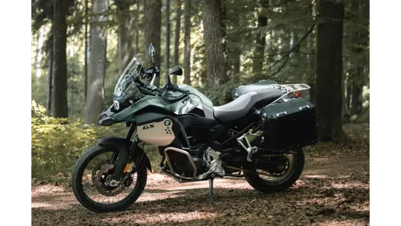 Zielony motocykl BMW F900GS z kuframi, gotowy na przygodę w lesie.