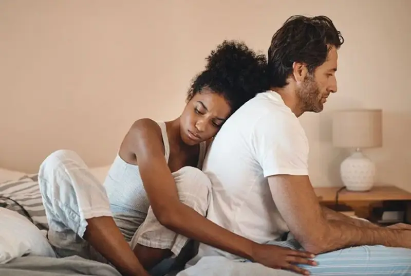 Un couple assis dos à dos sur un lit, l'air distant. On ne peut plus se parler sans s'engueuler.