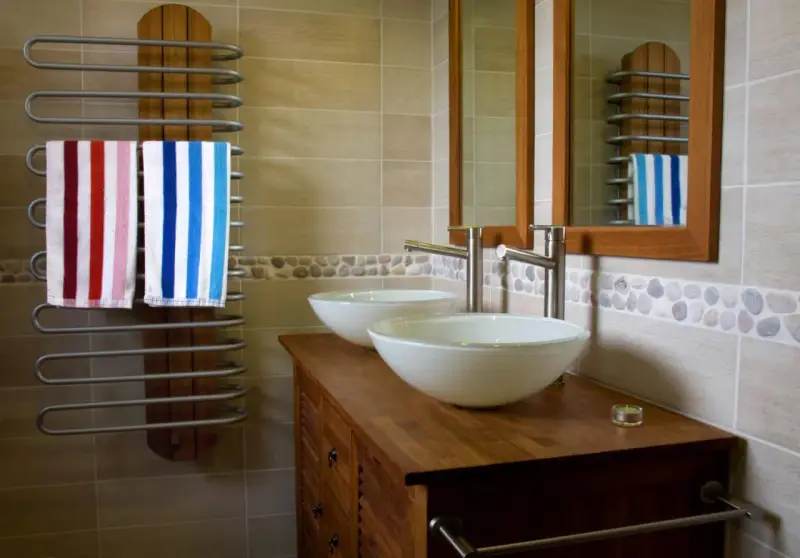 Salle de bain moderne avec double vasque. L'arrivée d'eau est discrète, deux lavabos blancs reposent sur un meuble en bois. Deux serviettes rayées sèchent sur un radiateur.