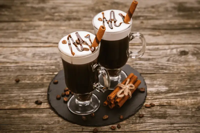 Dwa Irish coffee z bitą śmietaną, polewą czekoladową i laską cynamonu. Jaki to smak? Słodki, kawowy, z nutą alkoholu i przypraw.