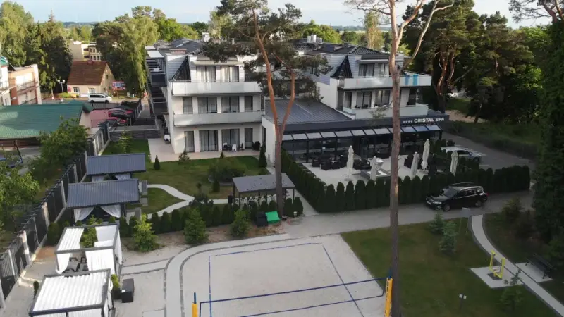 Nowoczesny hotel Cristal Spa z basenem i kortem do siatkówki plażowej, otoczony zielenią.