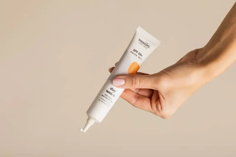 Dłoń trzyma tubkę kremu z filtrem SPF 50+, idealnego do codziennej pielęgnacji. To kwintesencja skinimalizmu – prostota i skuteczność.