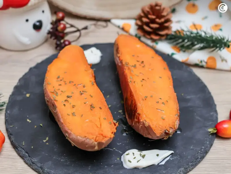 Dos mitades de boniato al horno, tiernas y doradas, con hierbas picadas y una cucharada de crema.