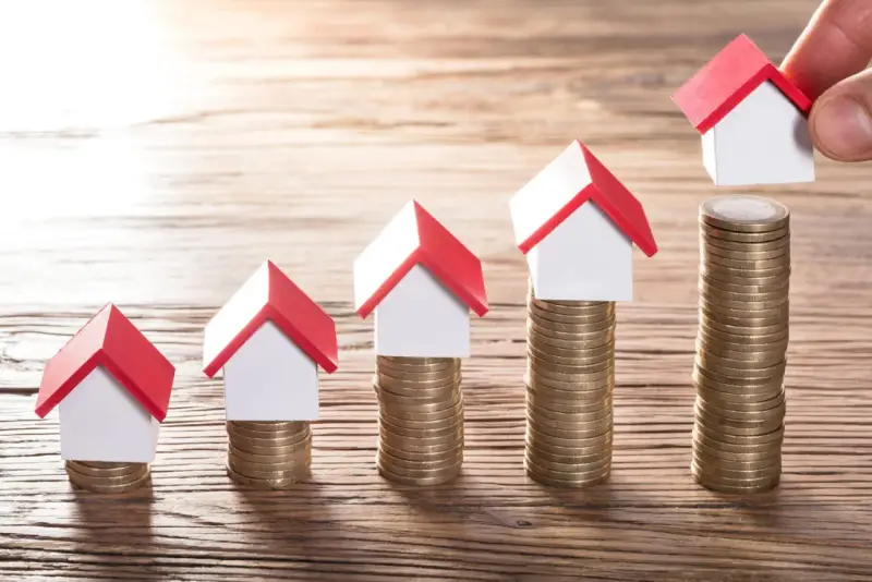 Cinq maisons miniatures sur des piles de pièces, symbolisant une augmentation du loyer sur 3 ans.