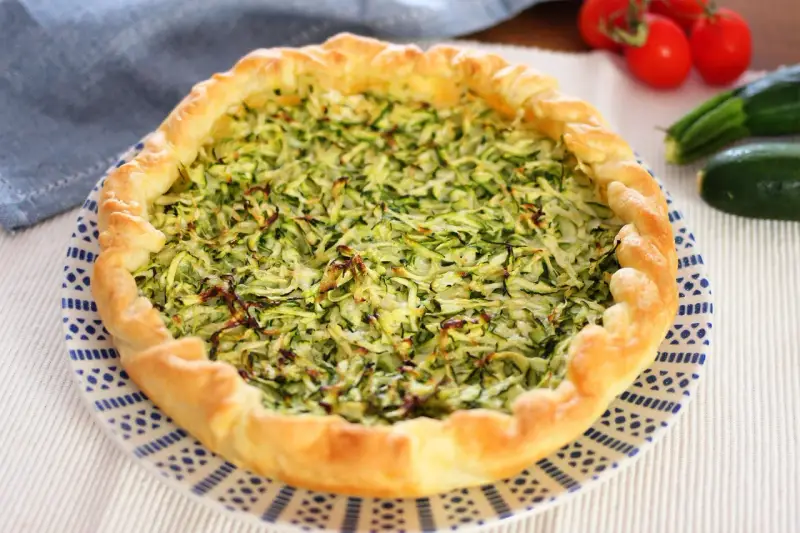 Torta salata con zucchine grattugiate e ricotta, con bordo dorato e decorazione blu su piatto bianco.