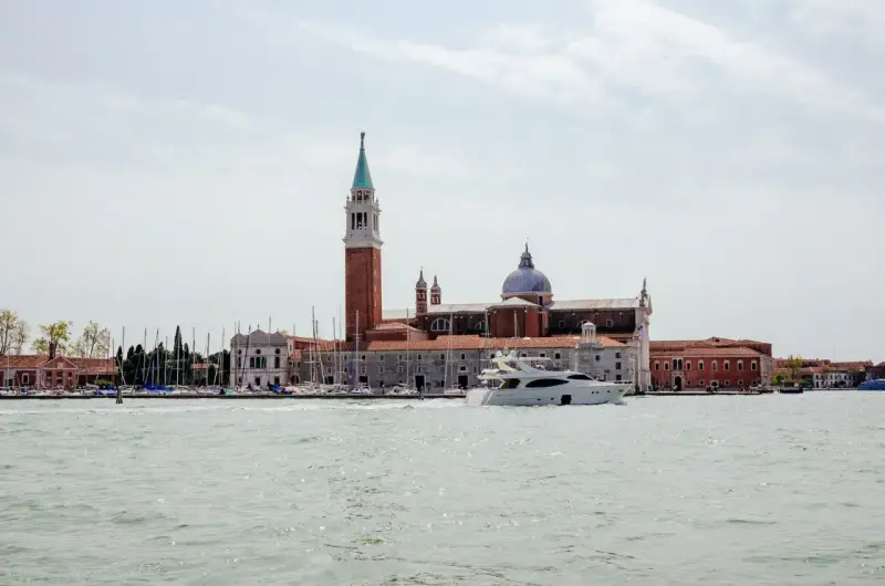 Un'isola di Venezia nascosta, con un campanile imponente, una chiesa con cupola e uno yacht che solca le acque.