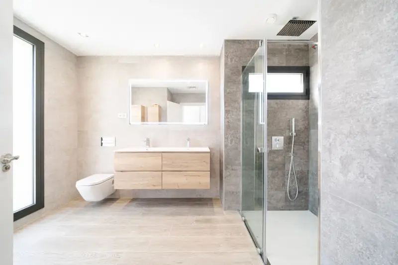 Baño moderno con ducha de cristal, lavabo flotante y WC suspendido. La fontanería se integra con estilo, cuidando cada altura y medida.