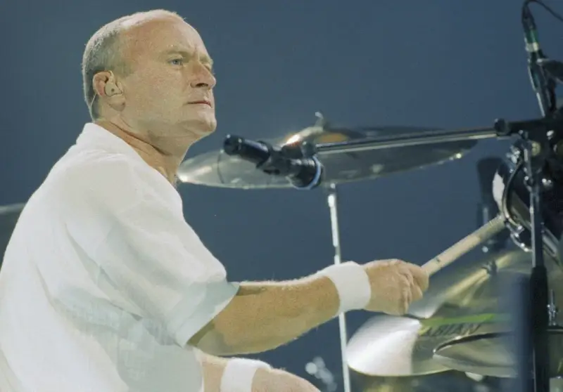 Phil Collins, w białej koszuli, gra na perkusji. Legendarny muzyk, znany z zespołu Genesis.