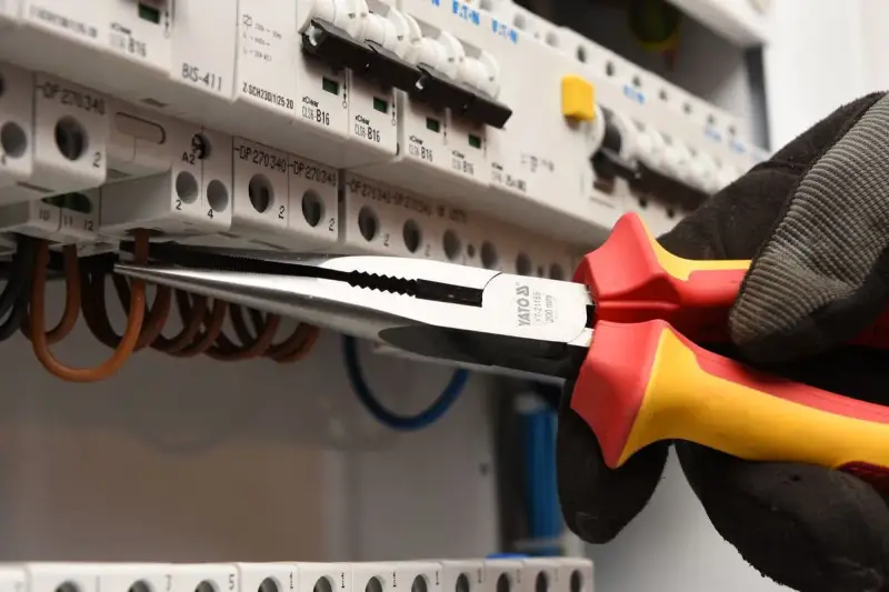Elektryk w rękawicy wymienia instalację elektryczną, używając kombinerki do przewodów w skrzynce z bezpiecznikami.