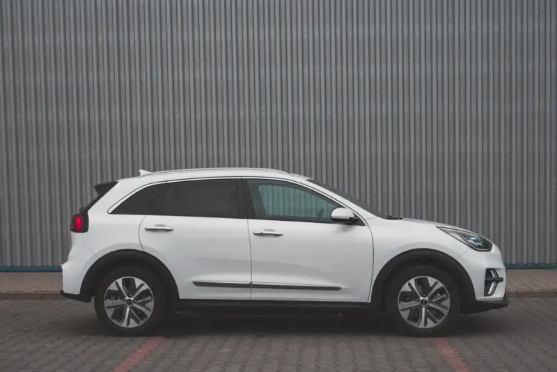 Biały Kia Niro EV widziany z boku na tle szarej, falistej ściany.