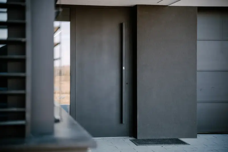 Nowoczesne, ciemnoszare drzwi zewnętrzne z długą klamką. Sprawdź montaż drzwi zewnętrznych cena i wybierz idealne rozwiązanie dla swojego domu.
