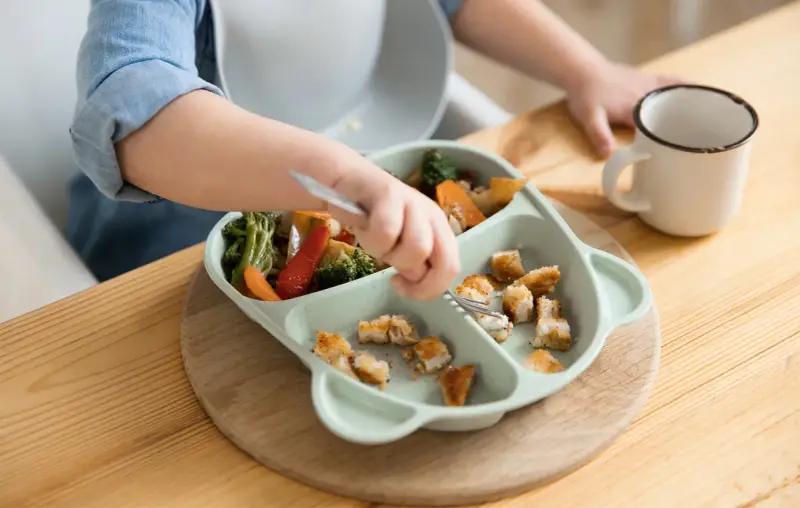 Małe rączki sięgają po kawałki kurczaka i warzyw. To pyszny obiad dla 2 latka, który uczy się samodzielnie jeść.