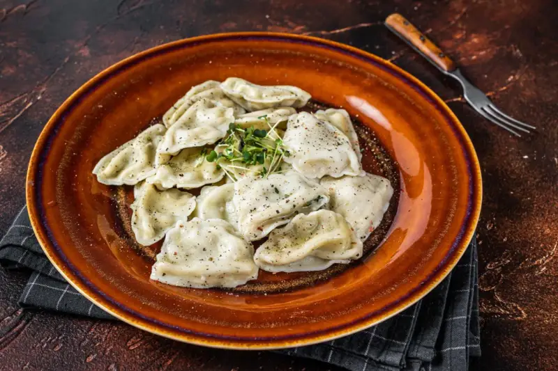 Talerz pełen pierogów, które przypominają o tradycji i pytają skąd pochodzą pierogi. Zioła dodają świeżości.