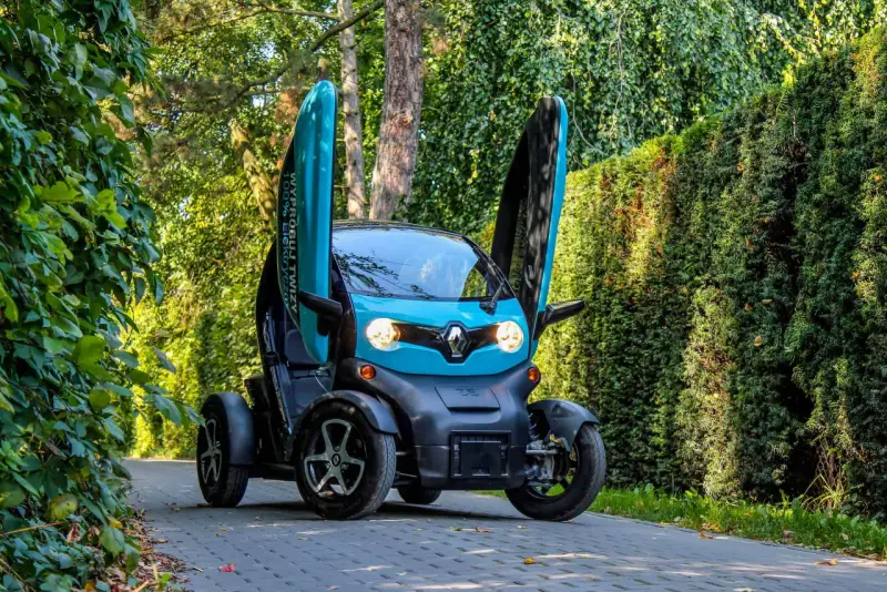 Niebieski Renault Twizy z otwartymi drzwiami stoi na ścieżce wśród zieleni.