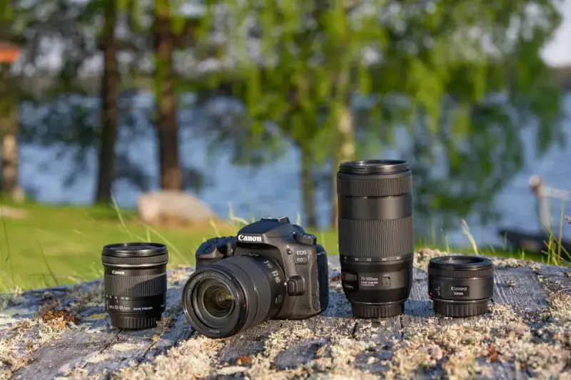 Aparat Canon EOS 90D z obiektywami 10-18mm, 70-300mm i 50mm na kamieniu nad jeziorem.
