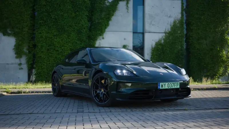Elegancki, ciemnozielony Porsche Taycan na tle zielonej ściany z bluszczu. Sprawdź aktualną porsche taycan cena i możliwości tego elektrycznego cudu.