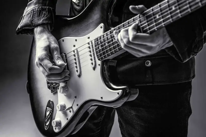 Ręce muzyka grające na gitarze do metalu. Czarno-białe ujęcie z bliska.