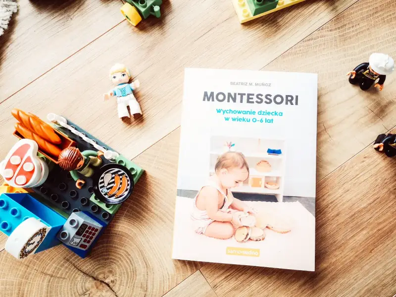 Książka "Montessori. Wychowanie dziecka w wieku 0-6 lat" obok klocków i figurek. Idealna do nauki przez zabawę.