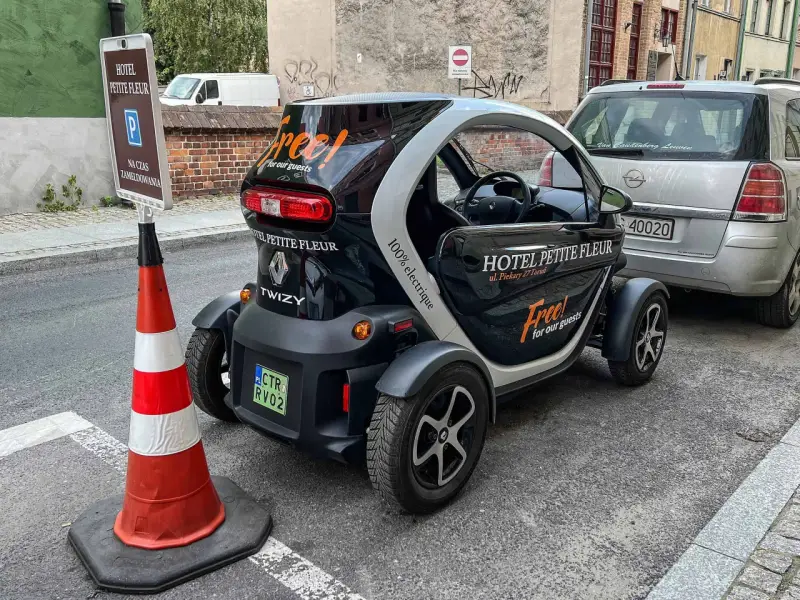 Czarny Renault Twizy z napisem "Free! for our guests" zaparkowany przed hotelem Petite Fleur. Obok znak parkingowy dla gości hotelowych.