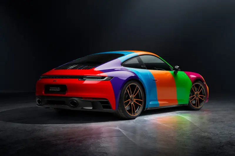 Porsche 911 Carrera GTS w tęczowym malowaniu, z pomarańczowymi felgami i odbiciami światła na podłożu.