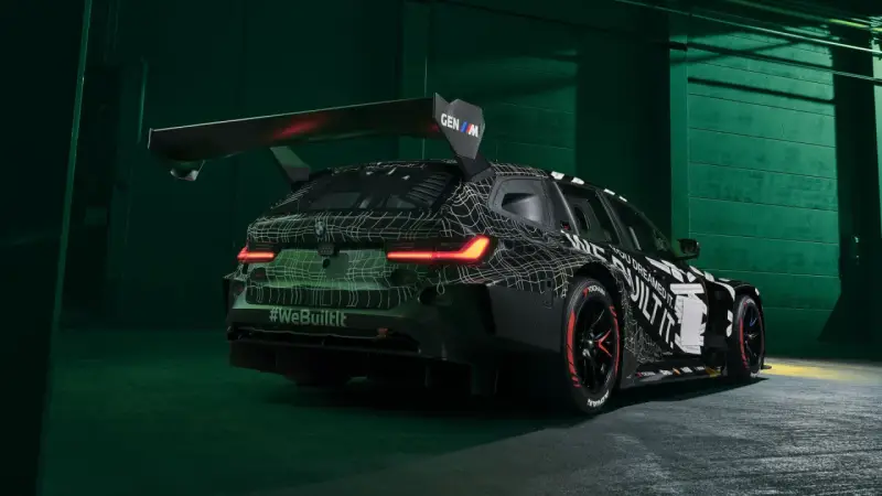 Wyścigowe BMW M3 2025 w kamuflażu, z ogromnym spojlerem i agresywnym dyfuzorem.