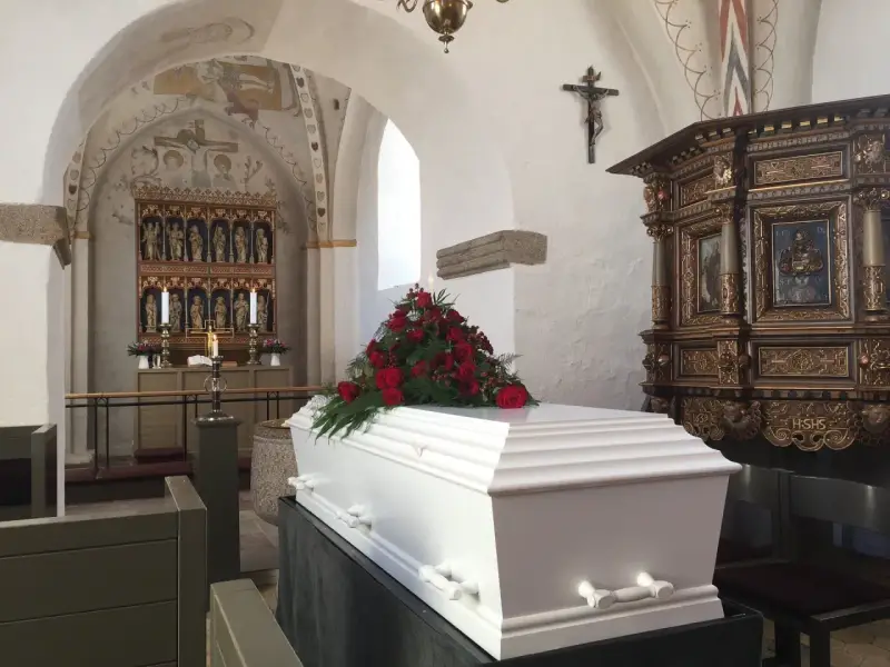 Biała trumna z czerwonymi różami w kościele. Warto wiedzieć, jak się zachować przy otwartej trumnie, by okazać szacunek zmarłemu.