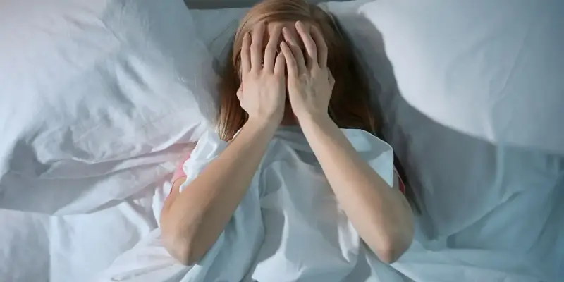 Dziewczyna w łóżku zakrywa twarz dłońmi, walcząc z bezsennością. Co to jest bezsenność?