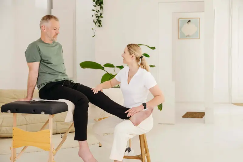 Physiotherapeutin hilft Mann mit Ischias-Schmerzen bei Dehnübungen. Sie streckt sein Bein, um die Nerven zu entlasten.