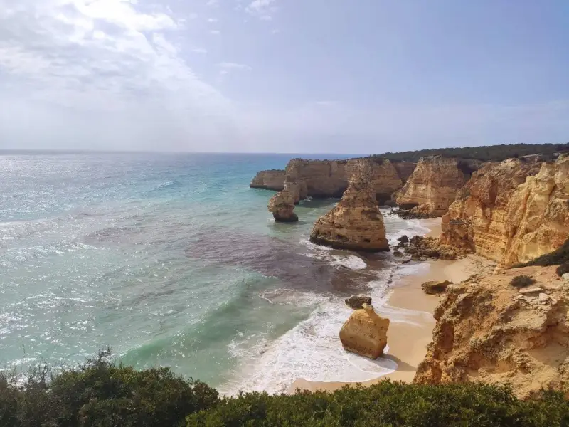 Acantilados dorados y mar turquesa en la ruta de los siete valles colgantes. Olas rompen en la arena de una playa escondida.