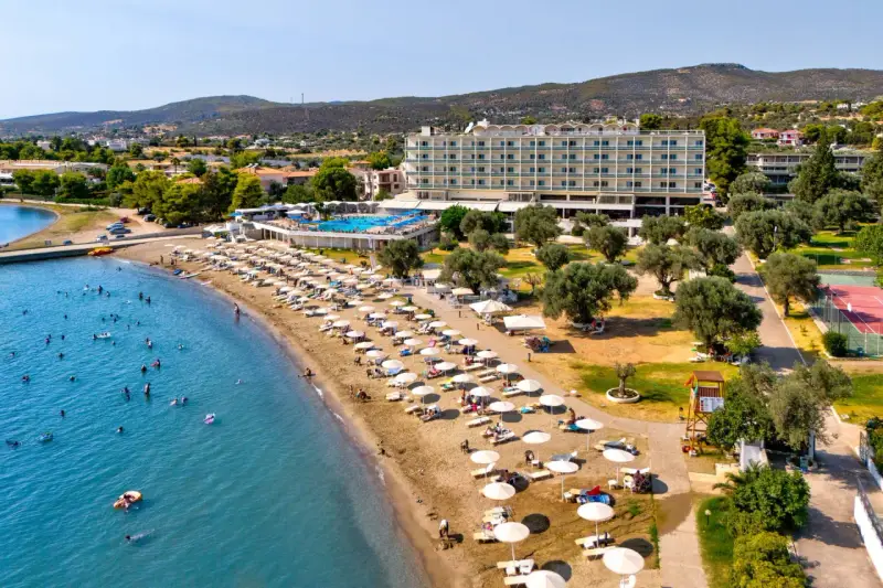 Piękna plaża na Evii, idealna na wycieczki fakultatywne. Hotel, basen, leżaki i mnóstwo ludzi kąpiących się w morzu.
