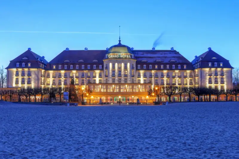 Elegancki Grand Hotel, część sieci luksusowych hoteli, lśni nocą na tle plaży.