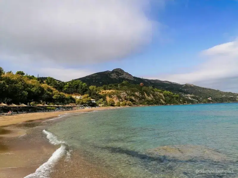 Piękna plaża Tragaki Zakynthos z turkusową wodą, zielonymi wzgórzami i rzędem leżaków pod parasolami.