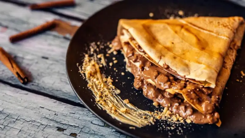 Crepe doblada con relleno cremoso de chocolate y trocitos de frutos secos. Ideal para aprender como hacer crepes deliciosos.