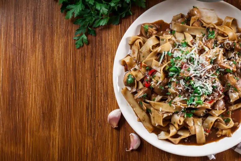 Pyszne danie z makaronem malfadine czy tagliatelle z grzybami i parmezanem, podane na drewnianym blacie.