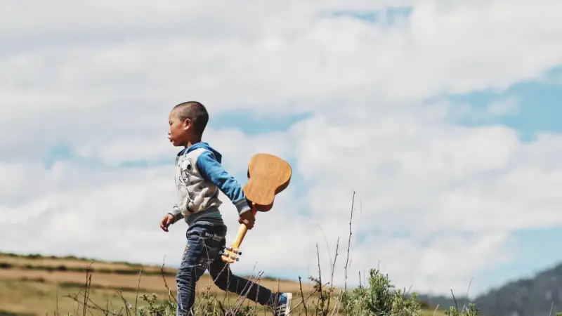 Ein kleiner Junge, vielleicht 18 Monate, rennt mit einer Ukulele durch die Natur. Ein sehr anstrengender, aber glücklicher Moment.