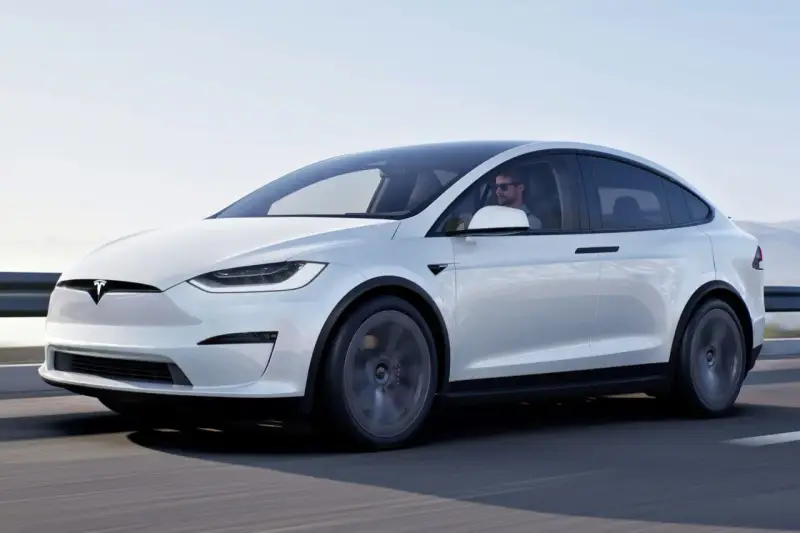Biały Tesla X w ruchu, kierowca w okularach. Zastanawiasz się nad jego ceną?
