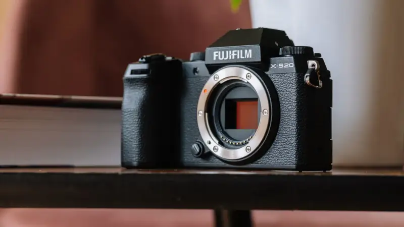 Czarny aparat Fujifilm X-S20 z obiektywem bez obiektywu, leżący na drewnianym stole obok książki.