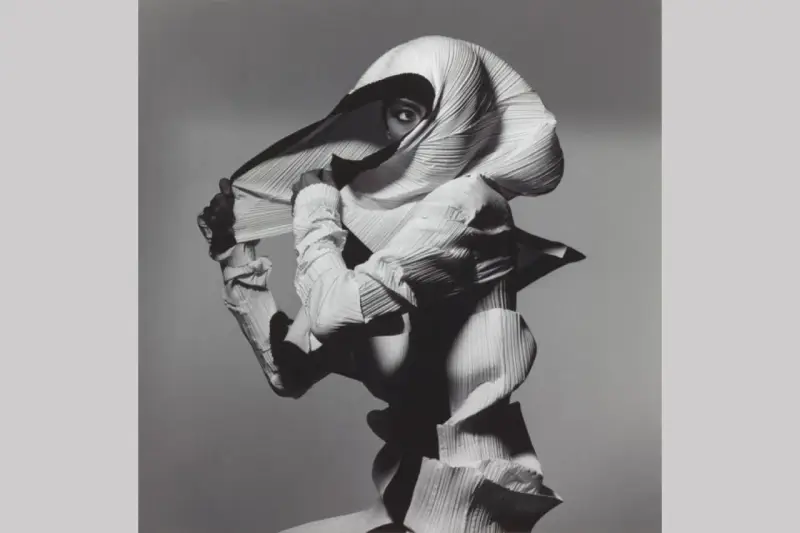 Modella con un abito plissettato bianco, un'opera d'arte di Irving Penn, che nasconde il viso tranne un occhio penetrante.