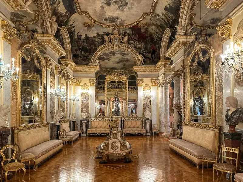 Złocone wnętrze pałacowe, przypominające muzeum w Madrycie, z malowidłami na suficie i bogatymi zdobieniami.