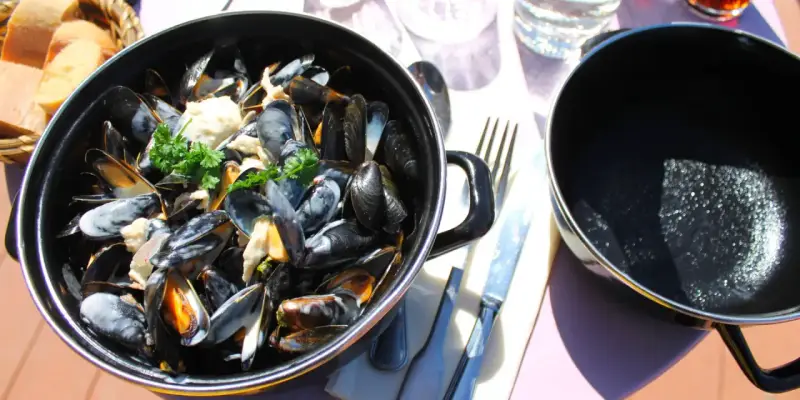 Moules marinières crémeuses, une spécialité culinaire normandie, servies dans une cocotte avec du pain frais.
