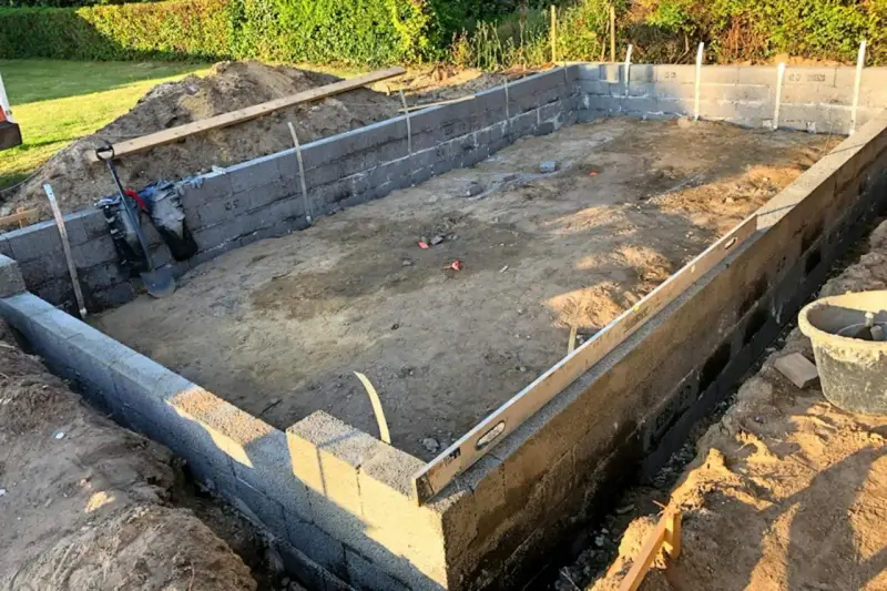 Byggarbetsplats med ett mura grund av betongblock. Schakt, spade och vattenpass syns.