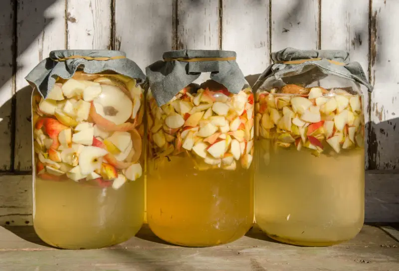 Trois bocaux remplis de pommes coupées, prêts pour la vinaigre de cidre recette de grand-mère.
