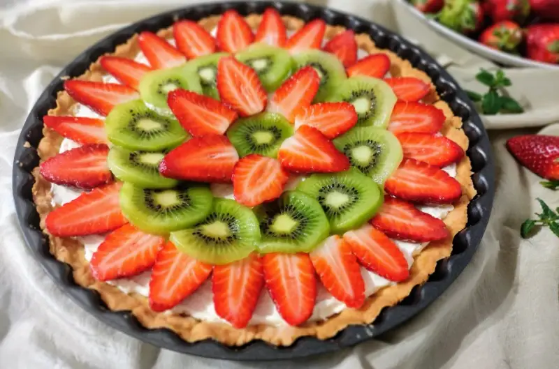 Kolorowa tarta z owocami: plasterki kiwi i truskawek ułożone na kremowym nadzieniu.
