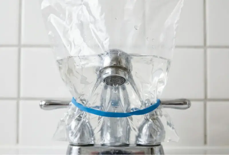 Un sac en plastique rempli d'eau est attaché à un robinet avec un élastique bleu. Une méthode pour enlever le calcaire de l'eau naturellement.